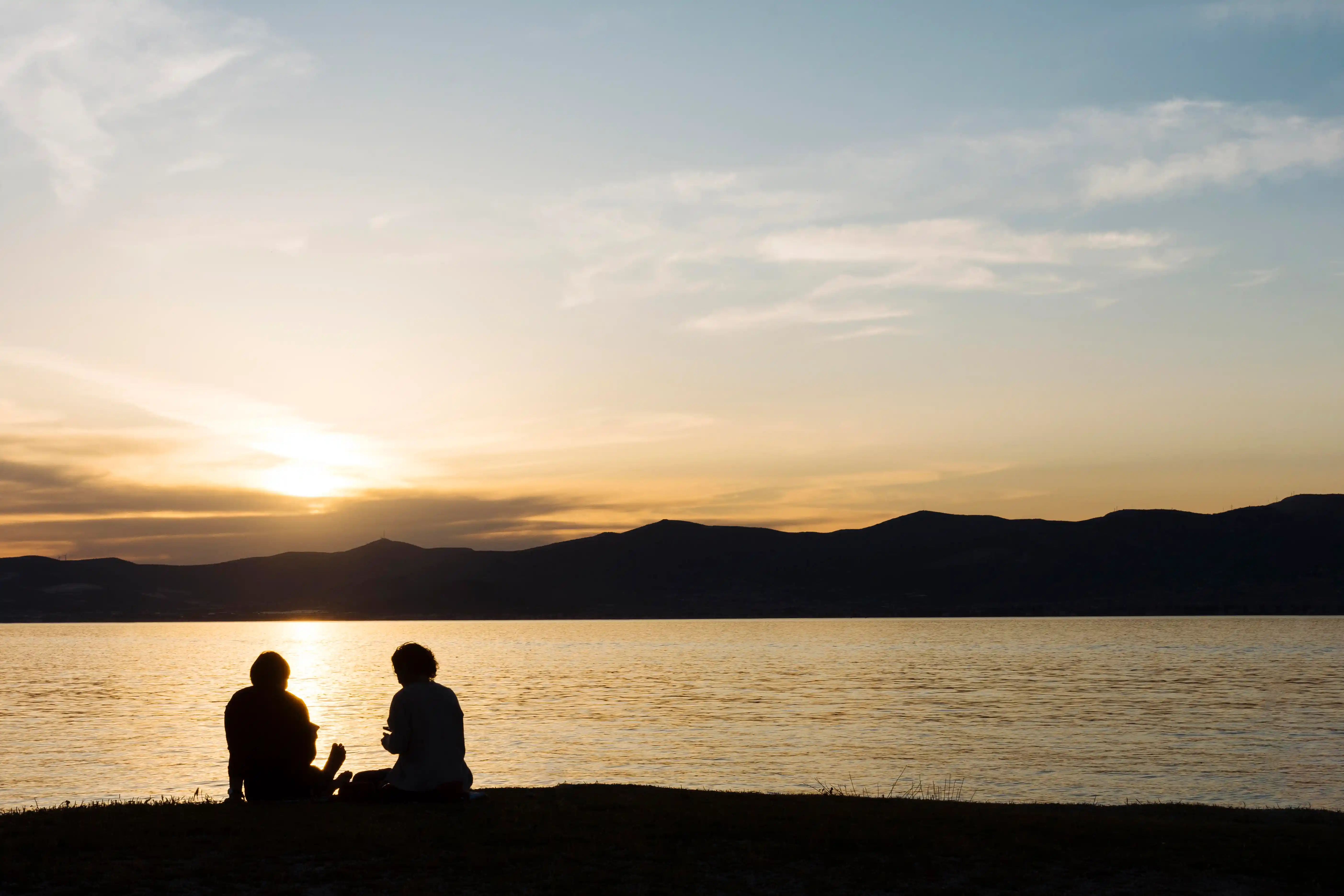 Silhouette of man and woman sitting on bench near body of water during sunset